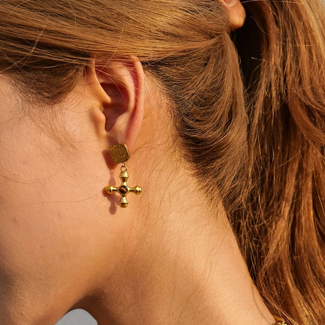 olivia le gold adalena earrings with square top detail with gold cross charm and brown stone on a model showing on her ear