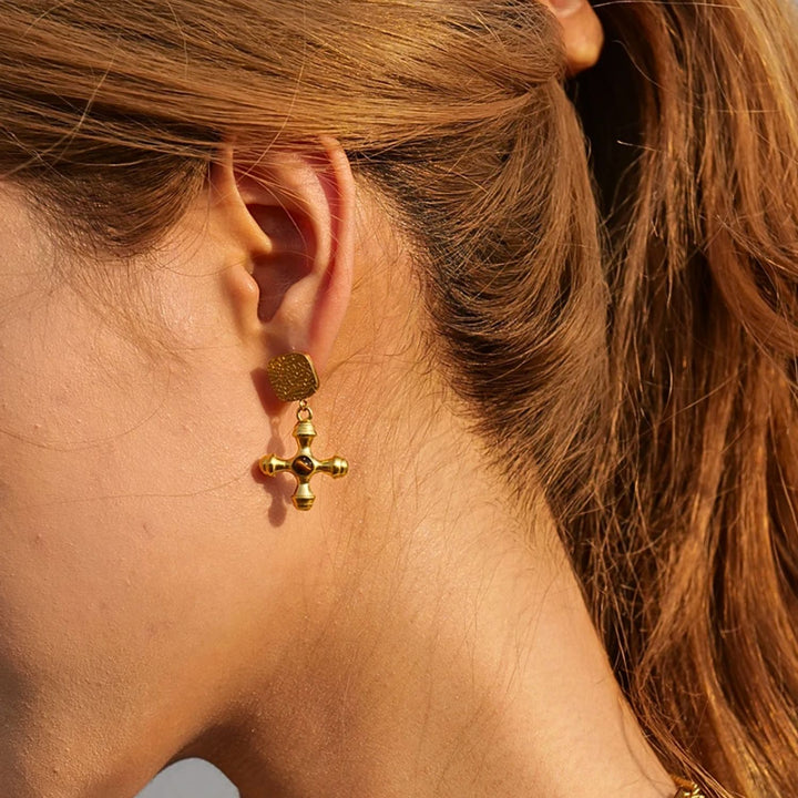 olivia le gold adalena earrings with square top detail with gold cross charm and brown stone on a model showing on her ear