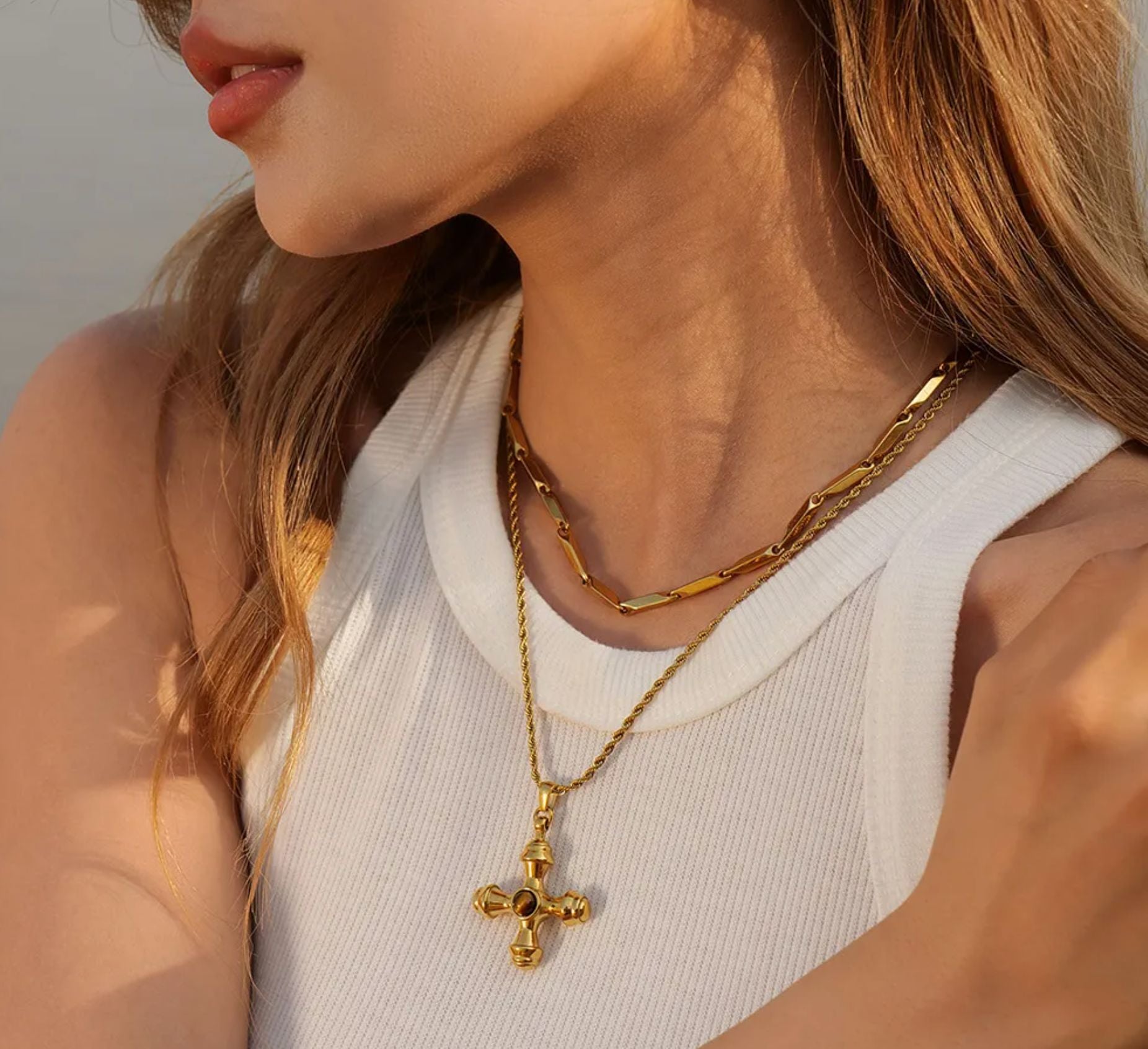 olivia le adalena gold cross pendant with brown tigers eye stone on a gold twisted rope chain model wearing it with a white tank top 