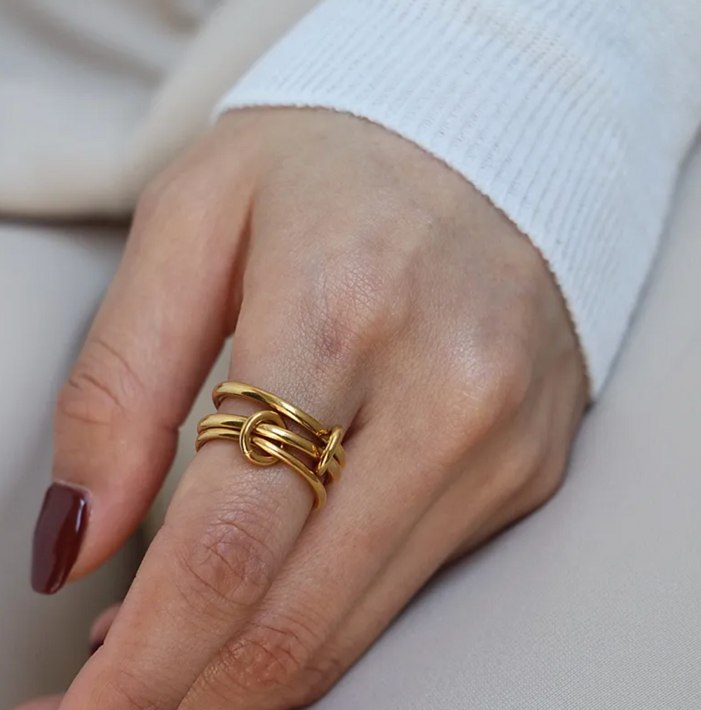 olivia le gold stacking ring that has 3 rings stacked connected with rings worn on a model with red nail polish