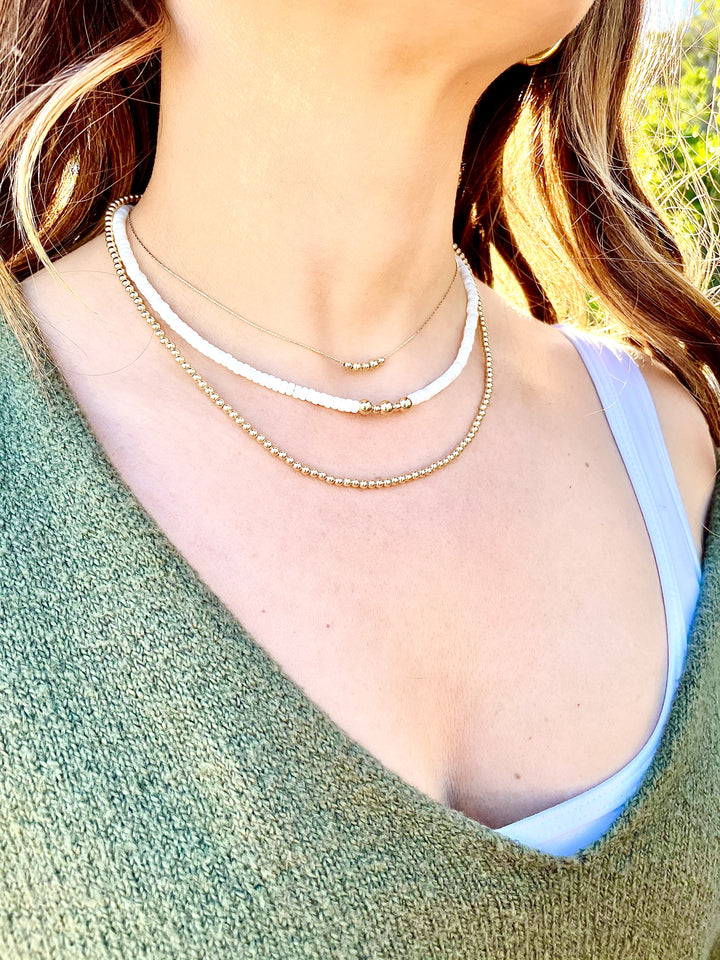Olivia le model wearing leilani mother of pearl necklace layered with 2 other necklaces with gold beads