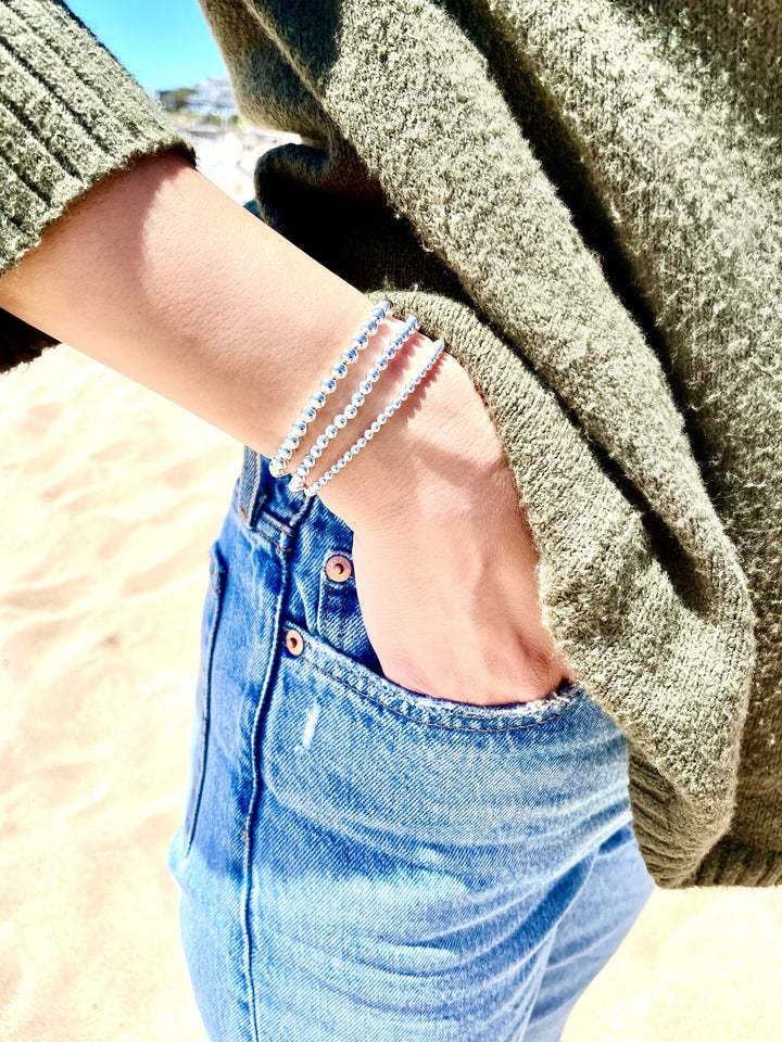 Olivia Le Model wearing 4mm sterling silver bead bubble bracelet on wrist while her hand is in her jean pocket and the bracelet is layered with the small and large size beads bracelets