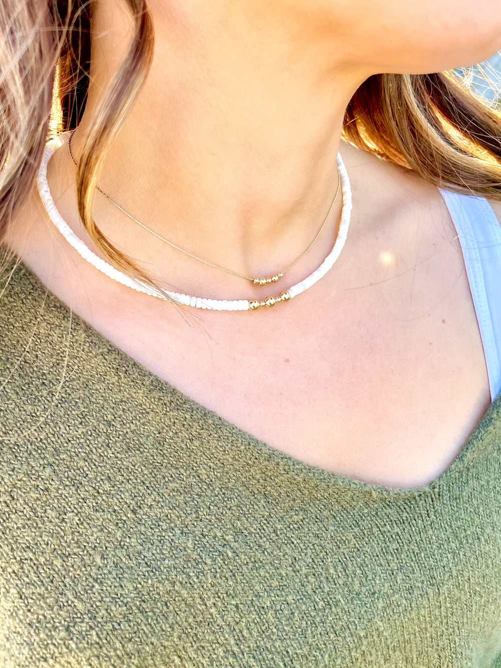 Olivia Le model wearing the brea bead necklace which consists of a thin gold filled beading chain with small gold beads in the front . the necklace is worn by the model with another necklace to showcase layering