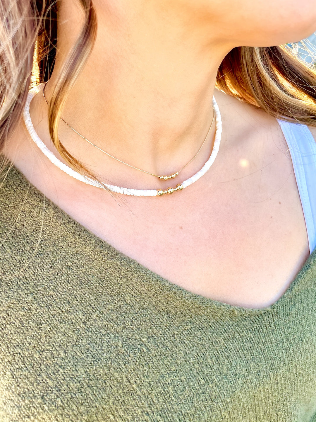 Olivia Le model wearing the brea bead necklace which consists of a thin gold filled beading chain with small gold beads in the front . the necklace is worn by the model with another necklace to showcase layering