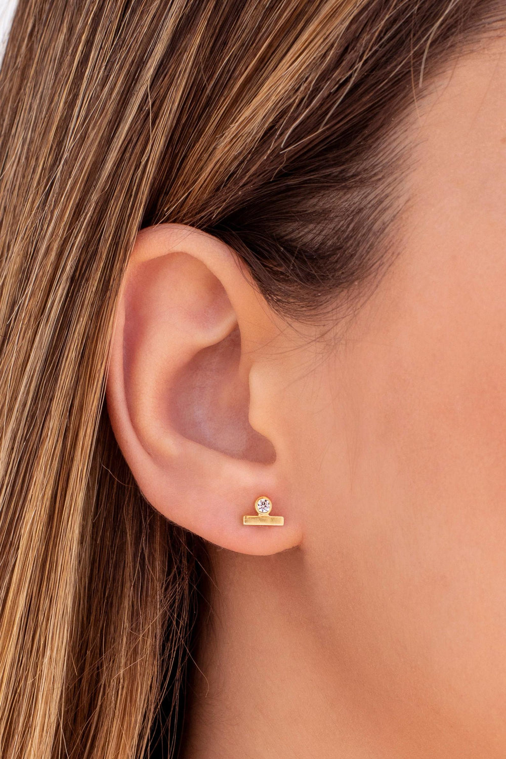 OLIVIA LE MODEL SHOWCASING EARRINGS ON HER EAR LOBE WEARING GOLD STUD NATALIA EARRING WITH CUBIC ZIRCONIA DETAIL AND BAR DETAIL