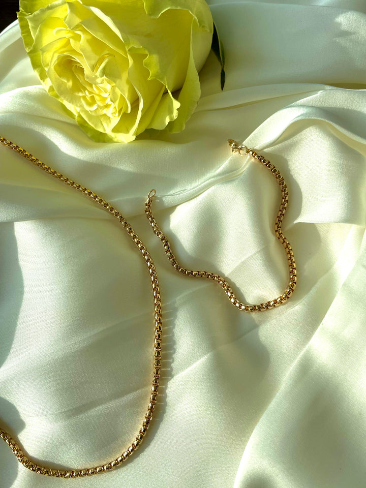 olivia le lifestyle image of devon chain necklace and bracelet laid on white fabric with a yellow rose 