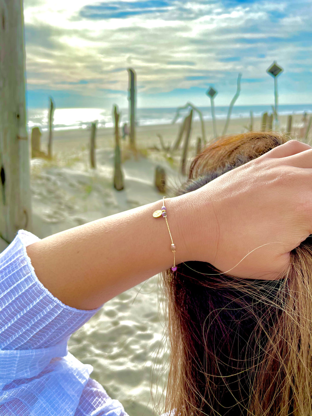 Olivia Le model at the beach wearing the Journey Phosphosiderite Beaded Bracelet with Coin pendant and white top