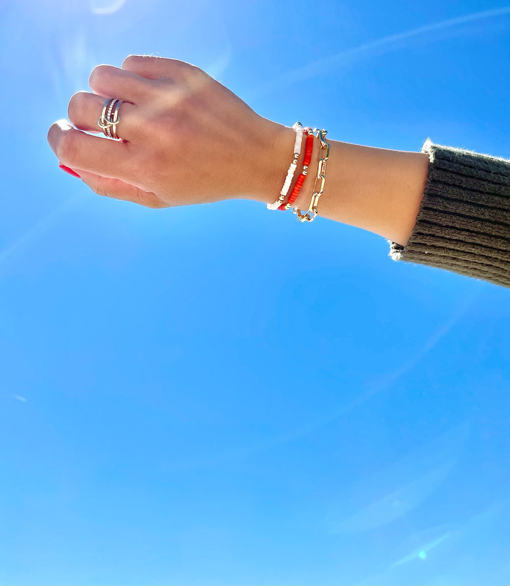 Olivia le model wearing linked up bracelet with mini harper and mini flora bracelets to showcase a layered stack bracelet look with her hand in the blue skies