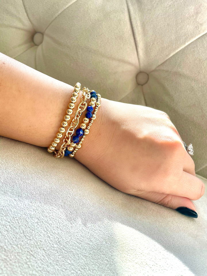 Gold bracelets layered on hand model showing multiple bracelets