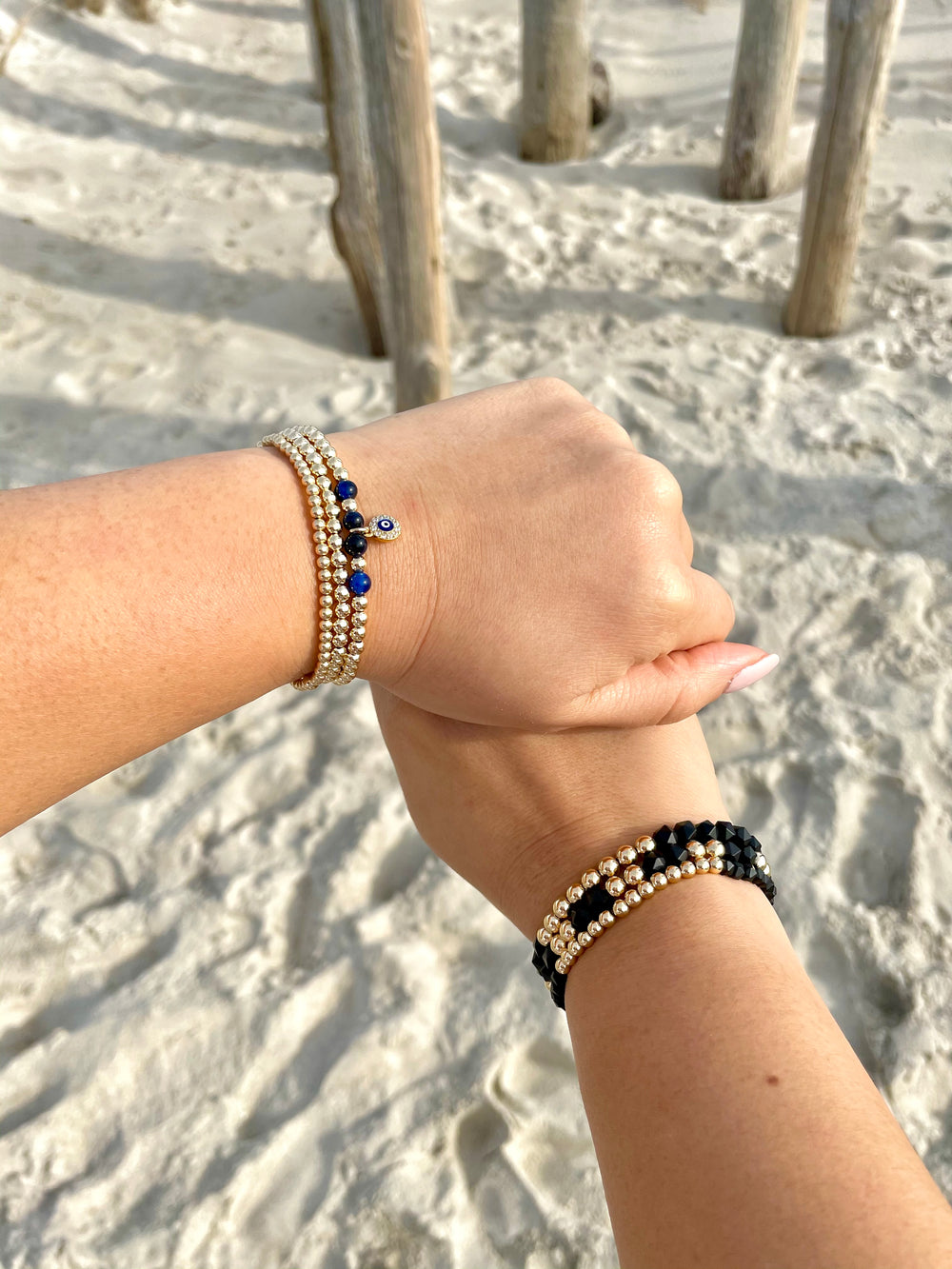Olivia Le models holding hands at the beach wearing a stack of gold-filled bead bracelets
