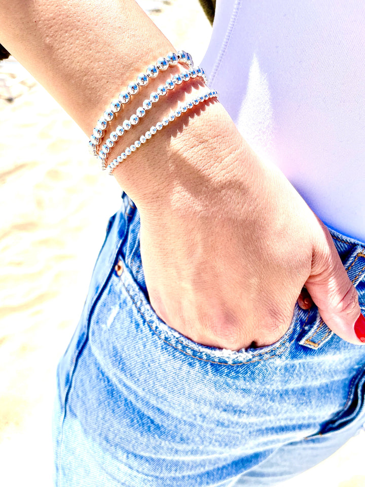 Olivia le model wearing the silver trip stack bracelets on her arm and her hand is modeling with her hand in the jean pocket showing off the bracelets