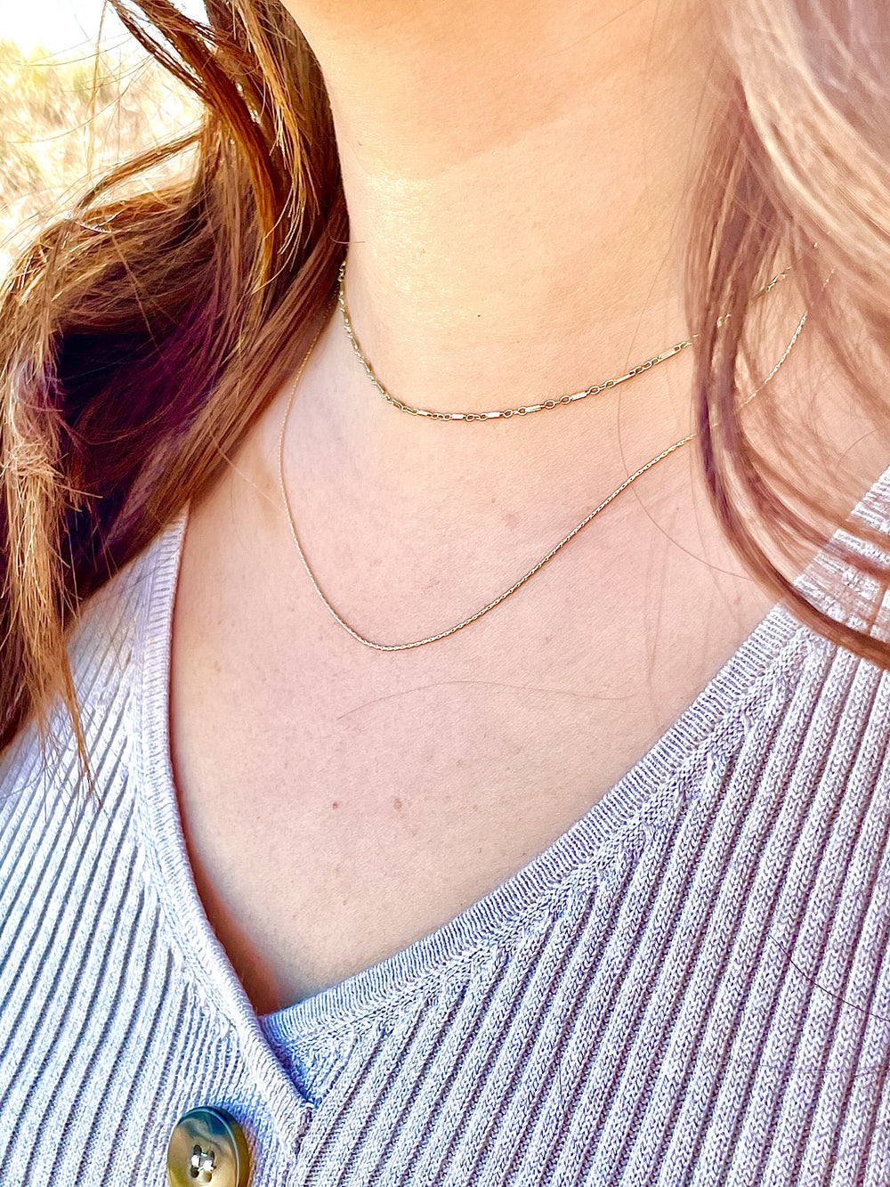Olivia Le model wearing the jayden stack necklace which has 2 dainty chains one of which is 14 inches and the second is 17 inches long on  v neck sweater