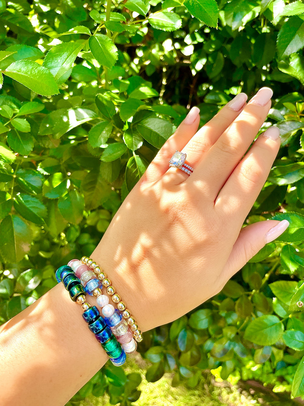 olivia le astra glass bead bracelet on model shown on models wrist with pale blue and pale pink glass beads with pearls and gold beads on elastic bracelet showcased with two other bracelets that are glass and gold beaded