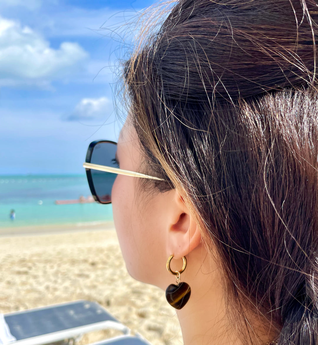 olivia le aubrey tigers eye heart hoop earrings shown on a model wearing the gold hoop earrings with a brown heart charm 