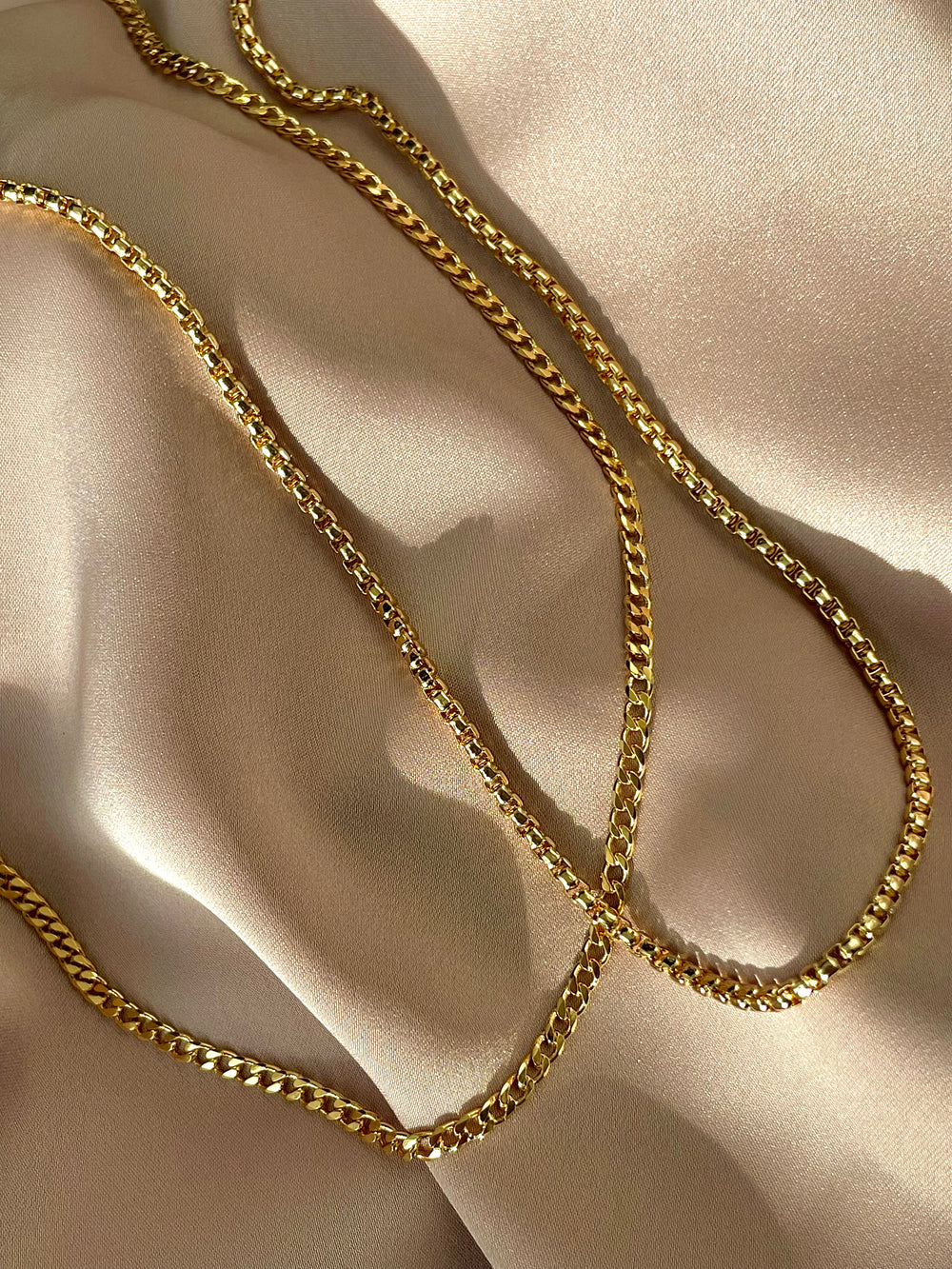 Olivia le candace curb chain shown laying flat on a pink satin fabric next to the devon box chain necklace