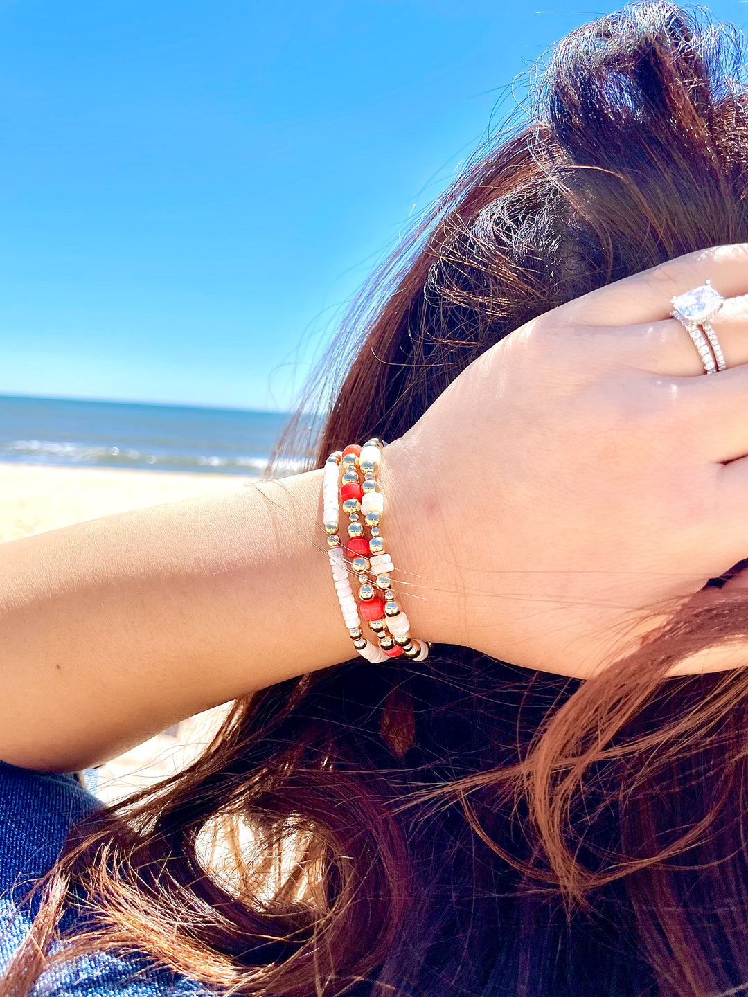 Olivia le model wearing the harper pearl bracelet on the beach with her hand posing on her head layered with the flora coral heishi bracelet
