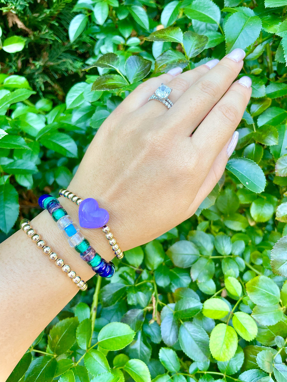 olivia le galaxy glass bead bracelet on model shown on hand with multicolored glass beads in blues and greens and purple mixed with gold beads shown with different bracelets to show layers