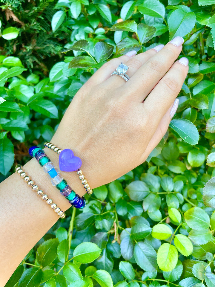 olivia le galaxy glass bead bracelet on model shown on hand with multicolored glass beads in blues and greens and purple mixed with gold beads shown with different bracelets to show layers