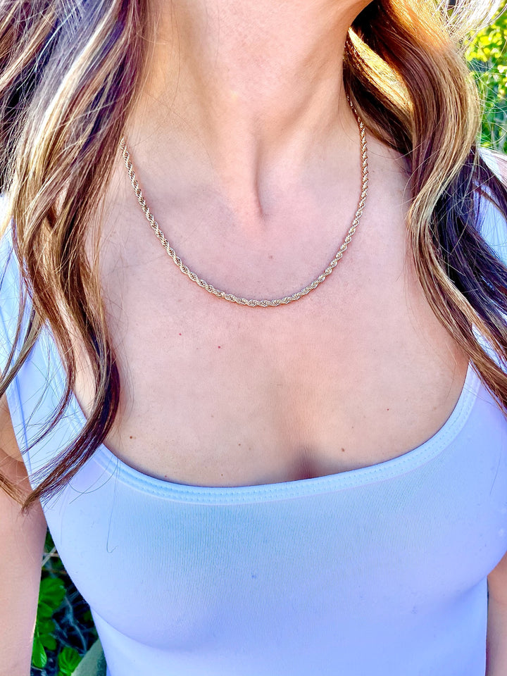 olivia le model wearing the grande venice rope necklace which is an 18k gold filled twisted rope necklace that is 20 inches long and model is wearing a white tank top 