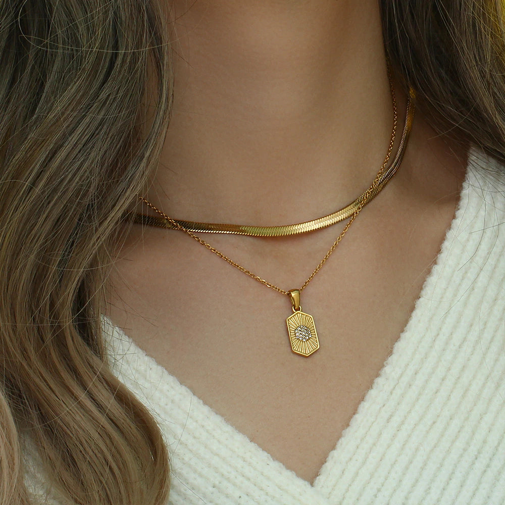 model wearing a white sweater and layered necklaces with olivia le odessa necklace hexagon pendant on the chain layered with herringbone necklace