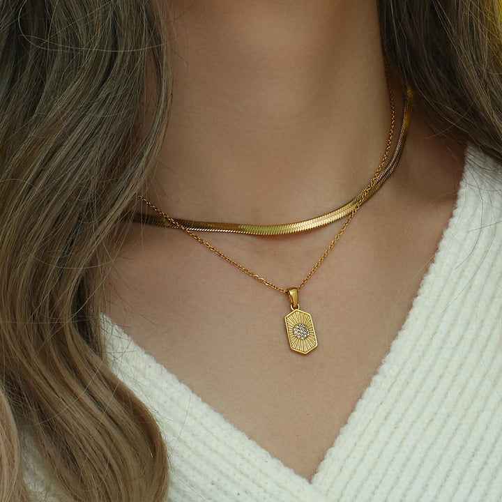 model wearing a white sweater and layered necklaces with olivia le odessa necklace hexagon pendant on the chain layered with herringbone necklace