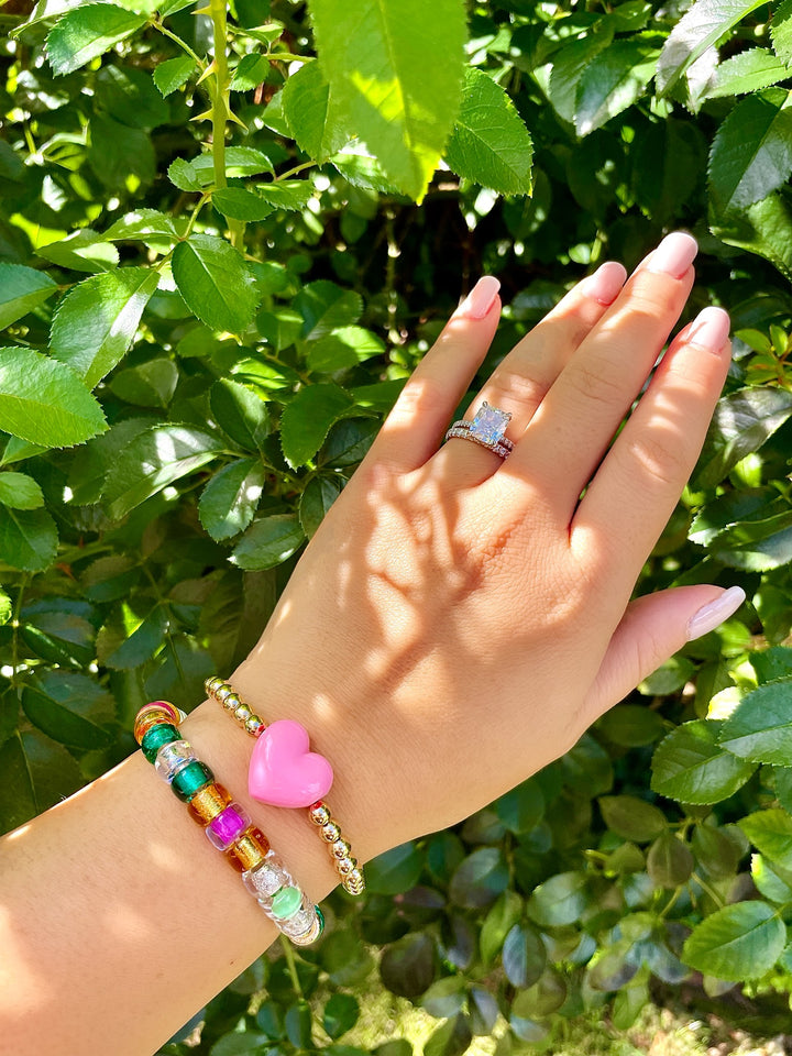 olivia le phoebe glass bracelet on model shown with green and gold beads with multicolors on a bracelet thats stretch layered with a heart beaded bracelet