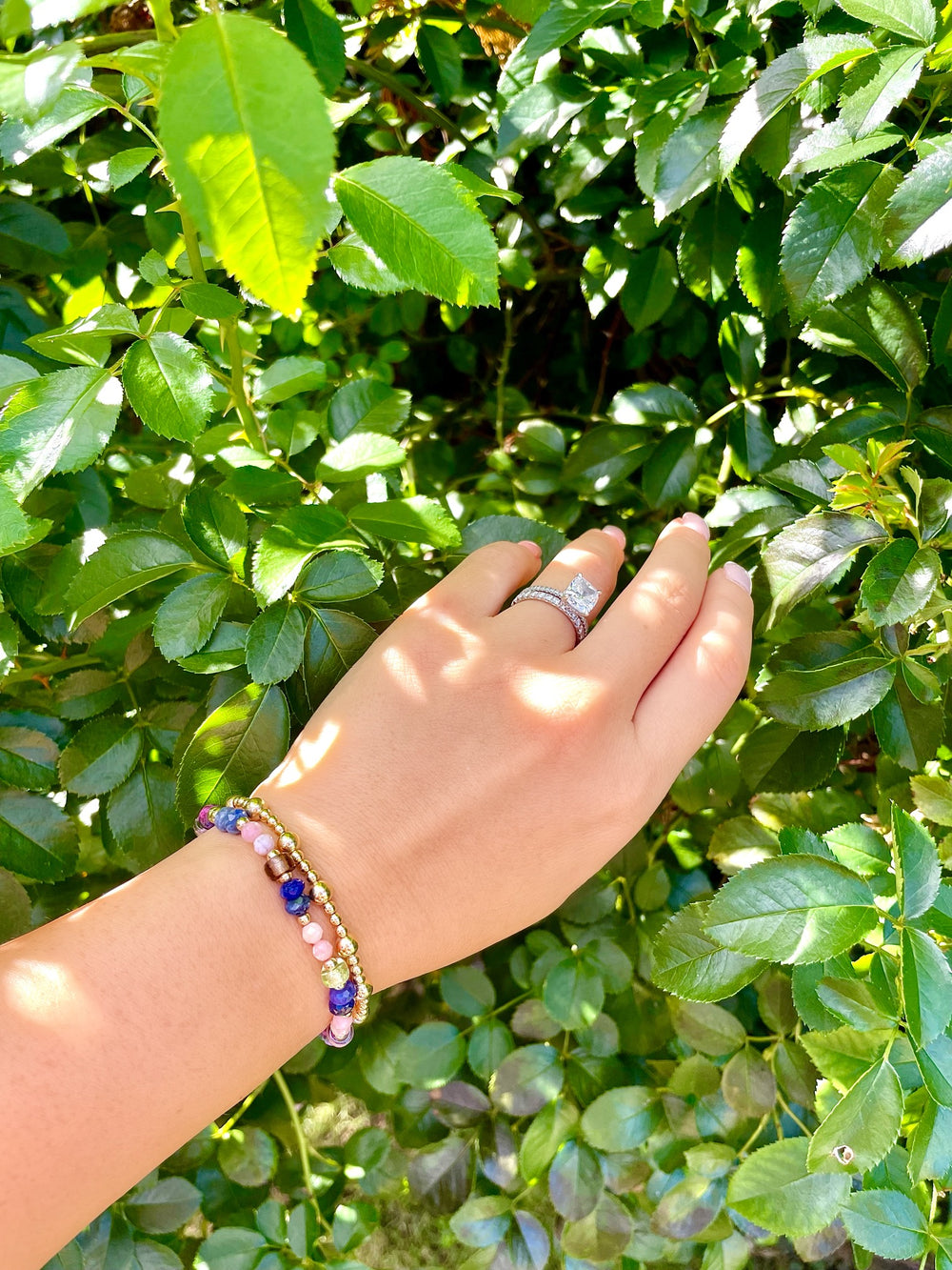 olivia le celine glass beaded bracelet on model hand showing purple brown pink and gold beads strung on a bracelet shown with another bracelet to show layered look 